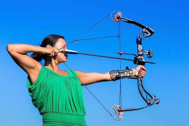 Young black haired woman aiming arrow of compound bow