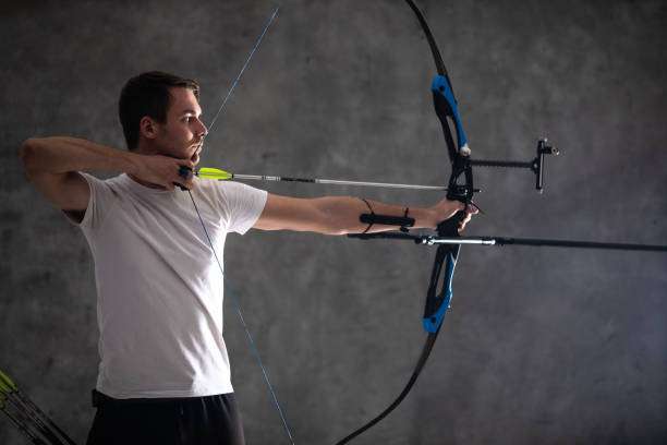 Male archer aiming with bow and arrow on gray background,compound bow