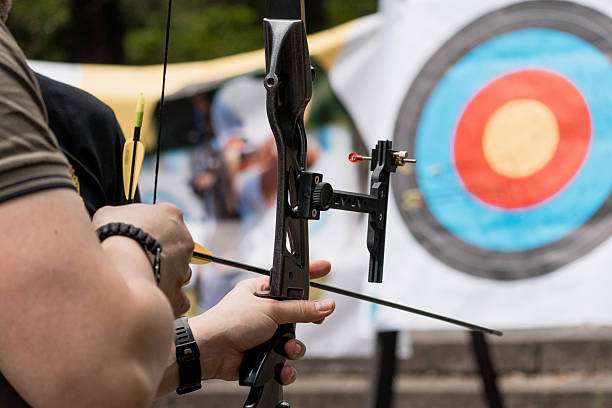 Young caucasian teenage boy practicing archery, shooting a red compound bow