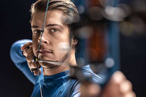 Young caucasian teenage boy practising archery shooting a red compound bow