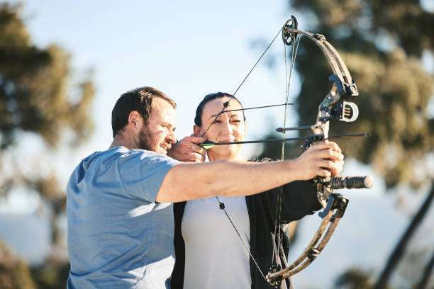A man with a prosthetic arm practicing archery with a compound bow on the field