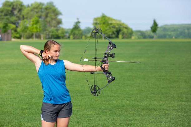 Teenage girl on archery training outdoors. Focus on the teenage girl's hands placing the arrow. playing a compound bow