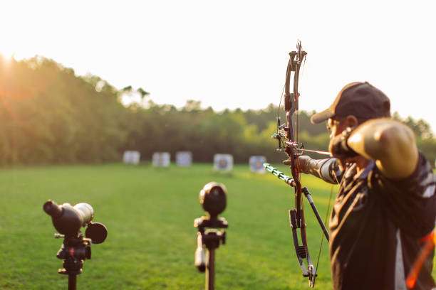 A man with a prosthetic arm practicing archery with a compound bow on the field