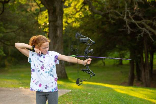 Young caucasian teenage boy practicing archery, shooting a red compound bow