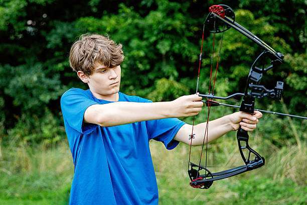 Teenage boy on archery training outdoors. Focus on the teenage girl's hands placing the arrow. playing a compound bow