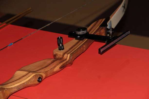 Close-up of a wooden compound bow riser with a black sight on a red background.