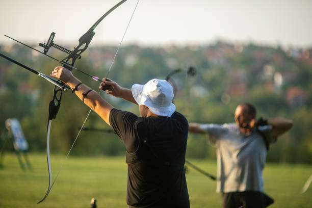 Archer in white hat aiming a compound bow outdoors.