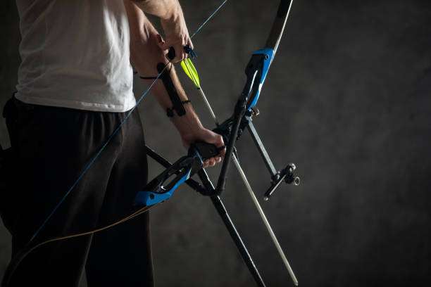 Archer loads a yellow arrow onto a blue compound bow in a dark setting.