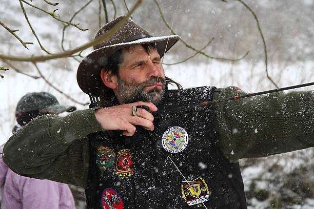 A male archer aiming a bow in the snow, practicing his technique for a compound bow.