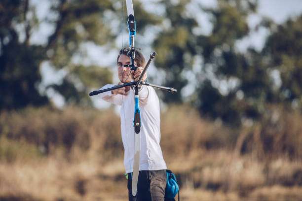 Archer aims a compound bow at a target in an outdoor setting.