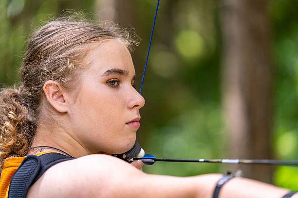 Young archer draws back arrow on compound bow.