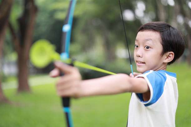 A man with a prosthetic arm practicing archery with a compound bow on the field in training at sunset. Focus on archer's face