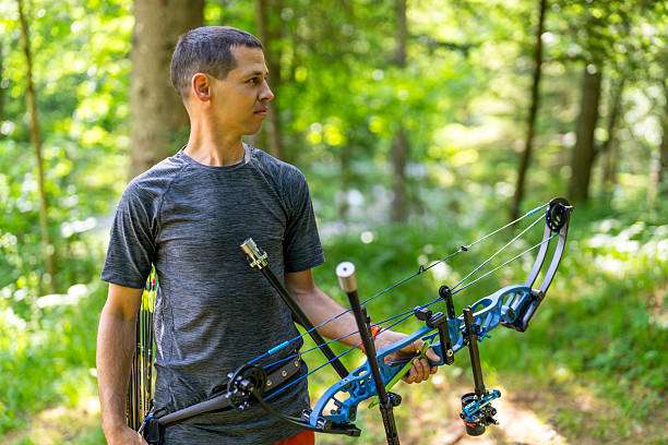 Man holds blue compound bow with arrows in a forest.