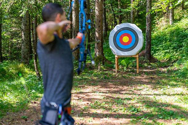 Man shoots compound bow at target in forest.