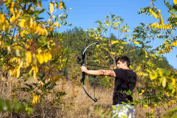 Young archer draws back a compound bow in a wooded area.
