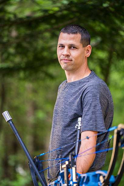 Man with compound bow, standing casually in nature.