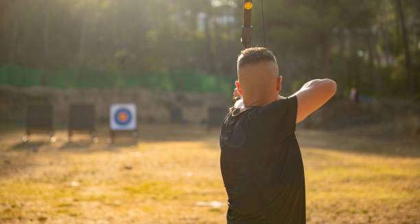 Archer draws back compound bow aiming at distant target.