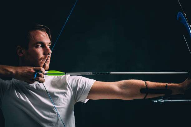 Focused young man in white shirt aiming a compound bow with blue strings.