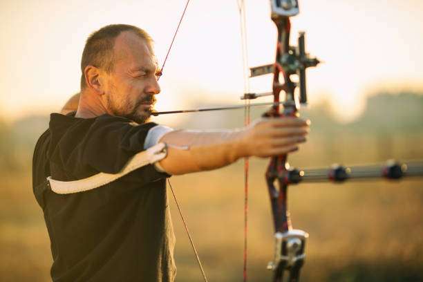 Focused man aims a compound bow at sunset.