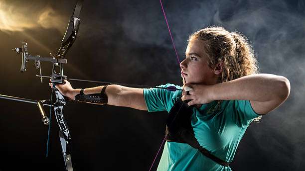 Teenage girl with curly hair aims compound bow.
